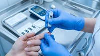 Healthcare professional in blue gloves using blood glucose meter for diabetes testing in medical clinic setting with monitoring equipment.