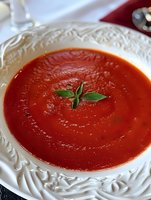 Fresh homemade tomato soup garnished with basil leaves served in an elegant white porcelain bowl with ornate relief pattern, close-up food photography.