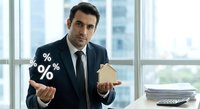 Professional businessman in suit holding percentage symbols and house model in modern office, representing mortgage rates and real estate investment decisions.
