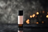 Small glass bottle with pink label on dark background with blurred golden bokeh lights. Minimalist cosmetic product photography for beauty brands.