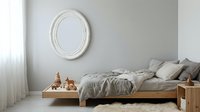 Minimalist bedroom interior with wooden bed frame, gray bedding, white round mirror on wall, and wooden toy blocks creating cozy Scandinavian style decor.