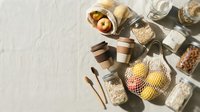 Flat lay arrangement of sustainable grocery items including fresh produce, grains, and reusable containers on white surface for eco-friendly shopping and zero waste lifestyle concepts.