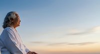 Senior woman with gray hair in white shirt gazing at sunset sky. Peaceful moment capturing contemplation and serenity during golden hour.