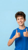 Happy teenage boy with curly hair showing thumbs up gesture in blue shirt on light blue background for youth marketing campaigns.