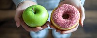 Hands holding green apple and pink glazed donut representing healthy versus unhealthy food choices for diet and nutrition decisions.