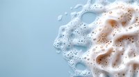 Creamy foam texture with bubbles and swirls on light blue background, macro photography showing abstract patterns and soft organic shapes in white and beige tones.