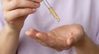 Professional applying golden serum oil from dropper bottle onto palm for skincare routine and beauty treatment application.