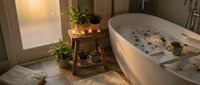 Luxurious spa bathroom with freestanding bathtub filled with flower petals, candles, and wellness products, wooden plant stand with greenery, soft lighting, and towels for relaxation and self-care.