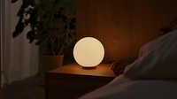 Glowing spherical lamp on wooden nightstand creates cozy warm atmosphere in dark bedroom interior, modern minimalist home decor lighting design.