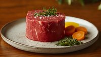Raw beef tenderloin steak garnished with fresh thyme on ceramic plate with sliced carrots, moody restaurant lighting and wooden table background.