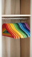 Colorful rainbow hangers arranged in spectrum order on closet rod creating organized wardrobe storage solution for home organization and decluttering.