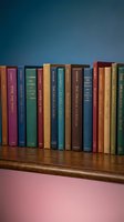 Row of vintage books on wooden shelf with colorful spines against blue wall background for education and literature concepts.