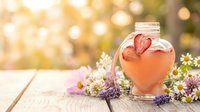Heart-shaped glass bottle with pink liquid surrounded by wildflowers and lavender on wooden surface with warm bokeh background for romantic themes.