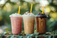 Three colorful iced coffee drinks with whipped cream and yellow straws on wooden surface with blurred green bokeh background for cafe menu design.