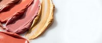 Creamy makeup foundation smears in coral pink and golden beige tones on white background for cosmetic advertising and beauty product campaigns.