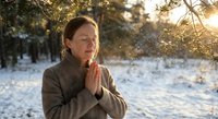 Peaceful woman meditating outdoors in snowy winter forest during golden hour sunrise, practicing mindfulness and yoga in serene natural setting.