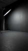 Professional photography studio setup with softbox lighting equipment on tripod stand, concrete floor and dark gray backdrop wall for product photography and commercial shoots.