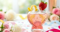 Heart-shaped glass filled with pink beverage garnished with fresh strawberry and lemon slice on romantic floral table setting for Valentine's Day celebration.