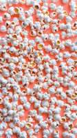 Fresh popcorn scattered on vibrant coral background, creating contrast between white fluffy kernels and bright color for food styling and advertising.