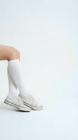 Young woman legs wearing white knee-high socks and classic canvas sneakers, minimalist studio shot on white background with copy space.