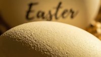 Textured Easter egg in warm golden tones with soft bokeh background and Easter inscription, cozy spring holiday celebration concept.