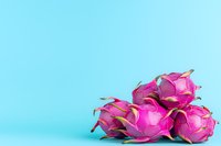 Fresh dragon fruit arranged on bright blue background, vibrant pink pitaya with green scales creating bold contrast, minimal food photography composition.