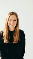Happy young Caucasian woman with long blonde hair wearing black sweater smiling at camera against neutral background for lifestyle and portrait use.