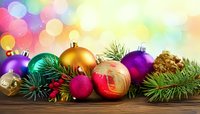Colorful Christmas ornaments and pine branches arranged on wooden surface against festive bokeh background.