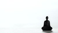 Minimalist black Buddha silhouette in meditation pose on clean white background for zen wellness and spiritual design projects.