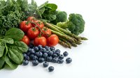 Fresh organic vegetables and blueberries arranged on white background including broccoli, cherry tomatoes, asparagus and leafy greens for healthy eating.