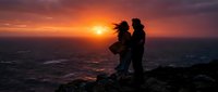 Silhouette of man holding child and woman standing together on rocky cliff overlooking ocean at golden sunset, family bonding moment.