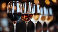 Wine glasses filled with different varieties from red to rose and white arranged in row against blurred warm lights background for wine tasting event.