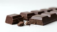 Dark chocolate bar broken into pieces with crumbs scattered on white surface, suitable for food photography, culinary content, and confectionery advertising.