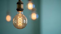 Vintage Edison bulb with glowing filament hanging from brass fixture against teal background with warm bokeh lights creating cozy atmospheric lighting.