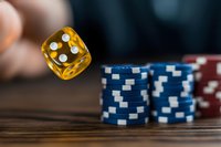 Yellow translucent dice rolling in mid-air above stacked blue and red poker chips on wooden surface, capturing dynamic casino gaming moment in macro photography.