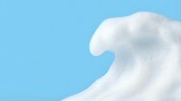 Dramatic white ocean wave crest against bright blue sky background creating dynamic natural seascape with powerful water motion and foam spray texture.