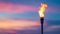 Bright gas flare burning against dramatic sunset sky with pink and blue clouds, industrial flame tower silhouette in dusk lighting creates atmospheric scene.