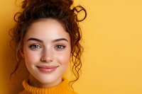Young woman with curly dark hair in yellow turtleneck sweater smiling warmly against vibrant yellow background, natural makeup and fresh glowing skin.