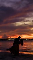 Romantic couple silhouette embracing at sunset beach with dramatic purple orange sky reflecting on water for wedding anniversary celebration.