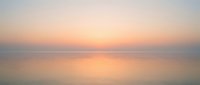 Serene ocean horizon at sunrise with soft peachy and golden light reflecting on calm water, creating a tranquil seascape for wellness and meditation projects.
