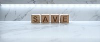Wooden letter cubes spelling SAVE on a marble surface with soft backlit white wall, symbolizing financial savings and money management concepts.