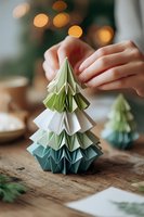 Hands creating origami Christmas tree in green and white paper with festive bokeh lights in background on wooden table.