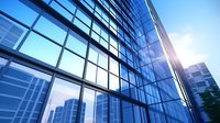 Modern glass office building facade with sunlight reflection creating geometric patterns against blue sky, showcasing contemporary urban architecture and sustainable design.