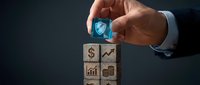Businessman hand placing security shield block on wooden cubes with financial icons representing data protection and business growth strategy.