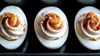 Deviled eggs topped with paprika and creamy filling, arranged in a row on dark surface for appetizer or party food styling.