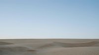 Vast desert landscape with rolling sand dunes under clear blue sky, minimalist natural scenery for travel and adventure content.