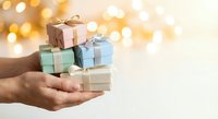 Hands holding a stack of pastel gift boxes with ribbons against a warm bokeh background, perfect for holiday and celebration concepts.