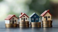 Small model houses in different colors placed on stacks of golden coins against blurred background, representing real estate investment and property market growth.