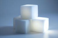 White sugar cubes stacked in minimalist composition against blue background, soft lighting creates gentle shadows and highlights pure crystalline texture.