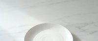 Empty white ceramic bowl on marble surface, isolated on clean background, suitable for food styling, restaurant menus, and tableware design projects.